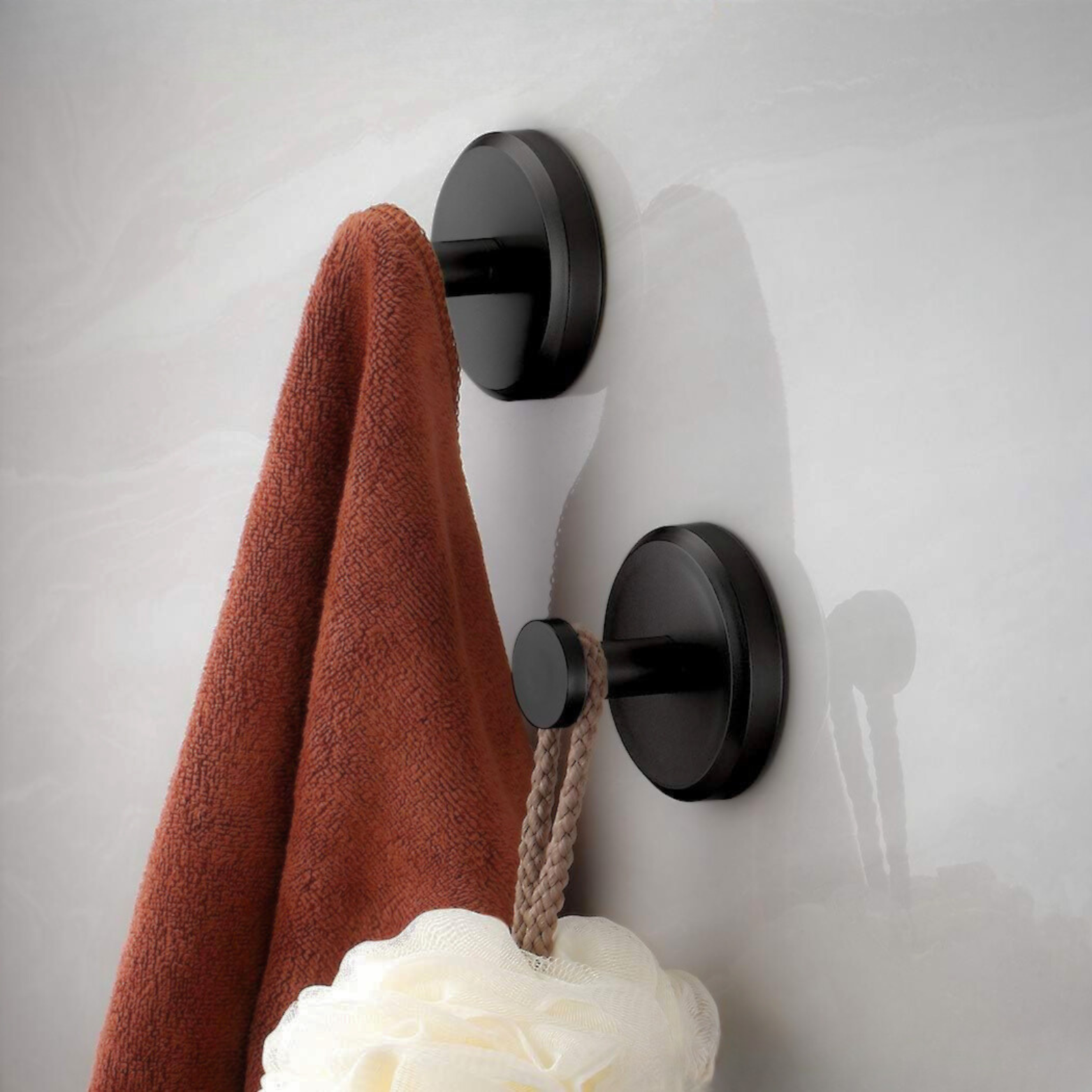 Ganci appendiabiti neri moderni su parete bianca con asciugamano marrone e spugna doccia. Accessori bagno eleganti e funzionali.