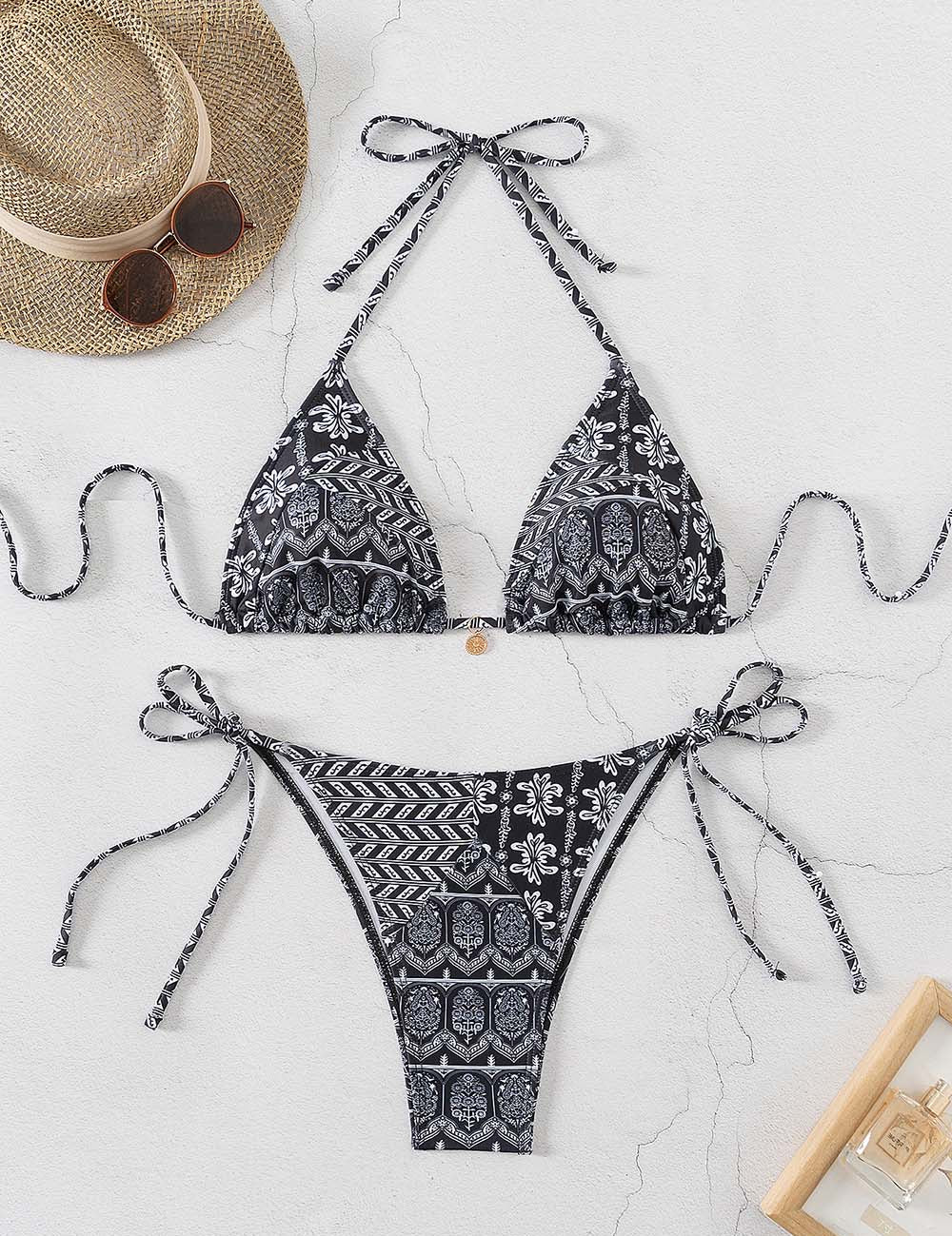 Bikini nero a fantasia floreale e geometrica, con laccetti regolabili. Accessori: cappello di paglia e occhiali da sole. Perfetto per l'estate.