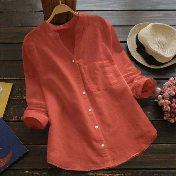 Camicia donna in lino rosso, maniche lunghe, colletto alla coreana, bottoni frontali, su tavolo di legno con cappello di paglia e fiori.