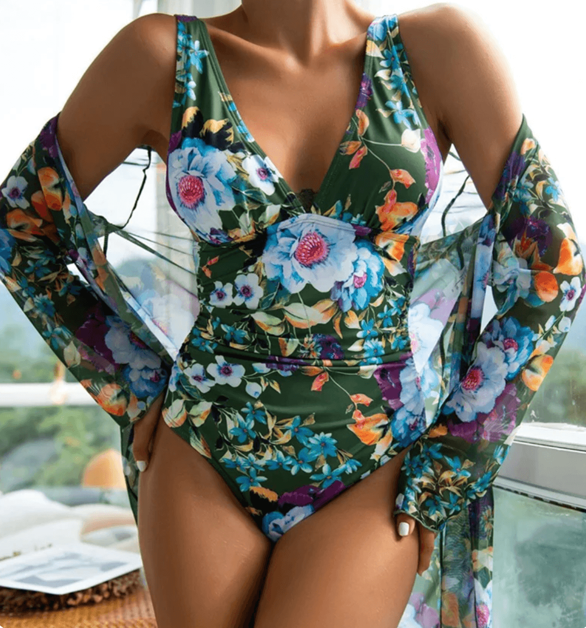 Costume intero floreale verde con scollo a V, abbinato a copricostume trasparente. Moda mare donna, abbigliamento estivo elegante e colorato.