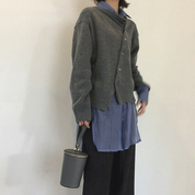 Maglione grigio asimmetrico su camicia blu, pantaloni neri, borsa a cilindro grigia. Moda casual autunnale, abbigliamento donna elegante.