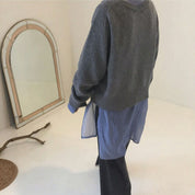 Maglione grigio oversize su camicia blu, moda casual autunnale. Specchio vintage e ramo decorativo sullo sfondo. Abbigliamento donna trendy.