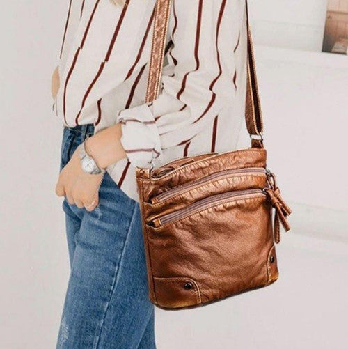 Borsa a tracolla in pelle marrone, design elegante con cerniere multiple, indossata da una donna con camicia a righe e jeans. Accessorio moda casual.