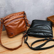 Borse a tracolla in pelle marrone e nera su tavolo di legno, design elegante con cerniere multiple, ideali per moda uomo e donna.