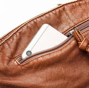 Borsa in pelle marrone con smartphone in tasca esterna con zip. Accessorio moda elegante, pratico per trasportare dispositivi mobili.