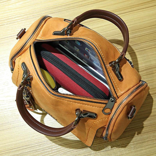 Borsa a mano in pelle marrone con zip aperta, contenente tablet, portafoglio rosso e accessori. Design elegante, ideale per moda e praticità.