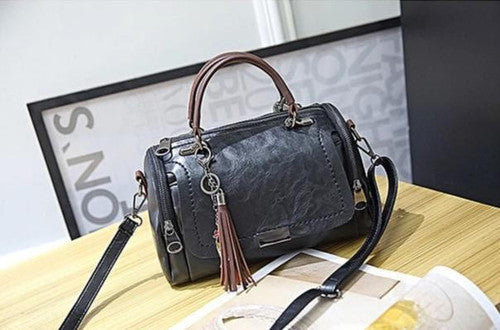 Borsa a tracolla in pelle nera su tavolo di legno, con manico marrone e ciondolo a frange. Design elegante, accessorio moda donna.