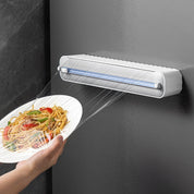 Dispenser automatico di pellicola trasparente su parete, avvolge un piatto di spaghetti con verdure. Utensile da cucina innovativo e pratico.