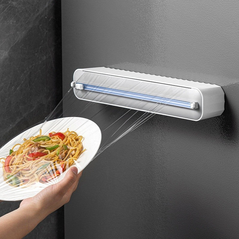 Dispenser automatico di pellicola trasparente su parete, avvolge un piatto di spaghetti con verdure. Utensile da cucina innovativo e pratico.