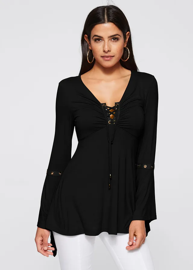 Donna con maglia nera a maniche lunghe, scollo a V con lacci, dettagli metallici, indossa pantaloni bianchi. Moda femminile elegante e casual.