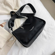 Borsa a tracolla nera in nylon su letto bianco, con cerniera argentata e cinturino regolabile. Design elegante, perfetta per moda casual e urbana.