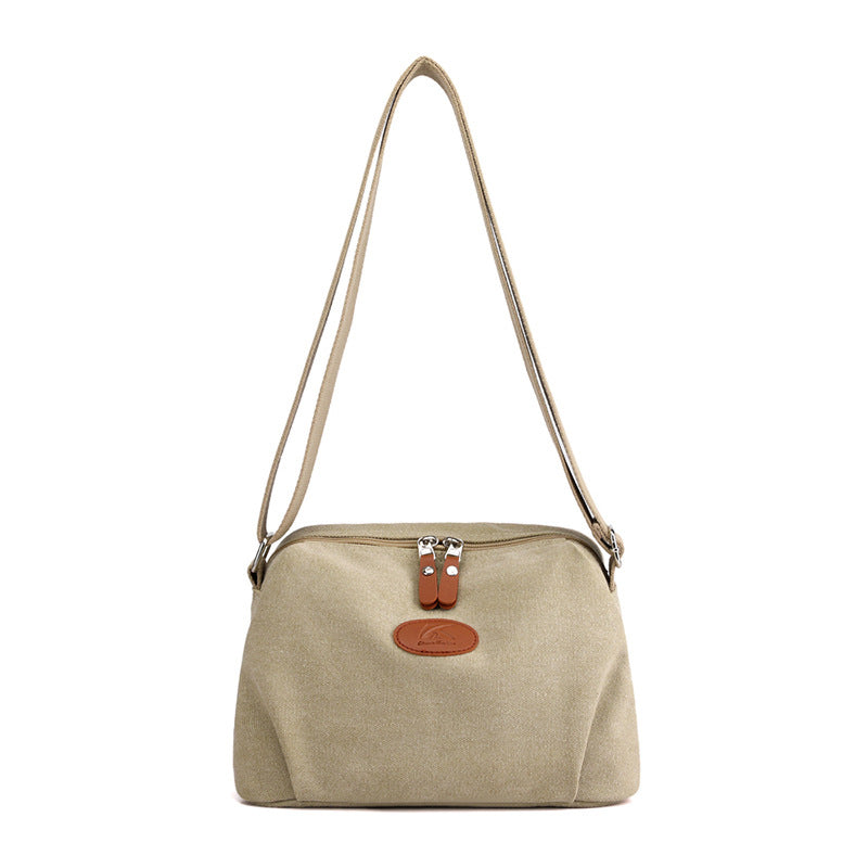 Borsa a tracolla beige in tela con chiusura a zip e dettagli in pelle marrone, design elegante e pratico per uso quotidiano.