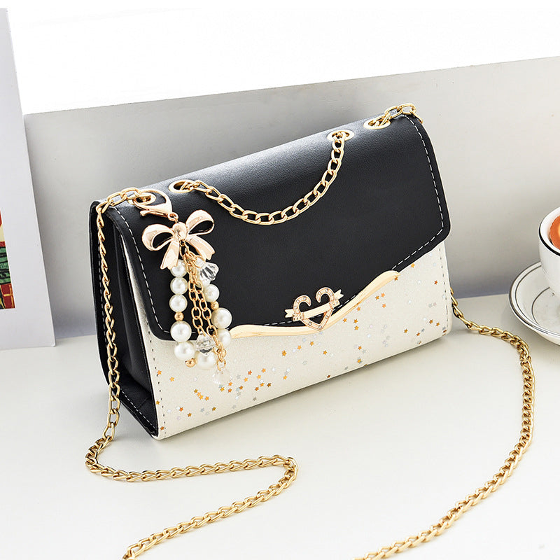Borsa a tracolla elegante in pelle nera e bianca con catena dorata, decorata con perle e fiocco. Accessorio moda donna, stile chic e moderno.