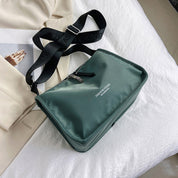 Borsa a tracolla verde in nylon su letto bianco, con cerniera e cinturino nero regolabile. Design moderno, ideale per moda urbana e viaggi.