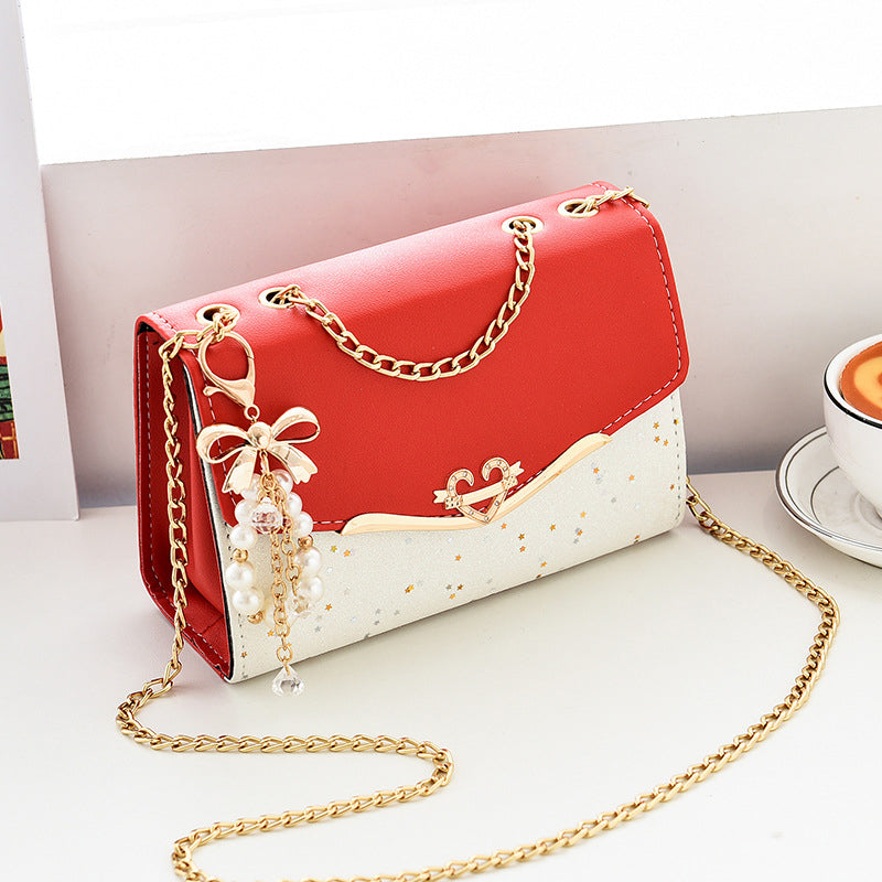 Borsa a tracolla elegante rossa e bianca con catena dorata, decorata con ciondolo perle e fiocco. Accessorio moda donna, stile chic e moderno.