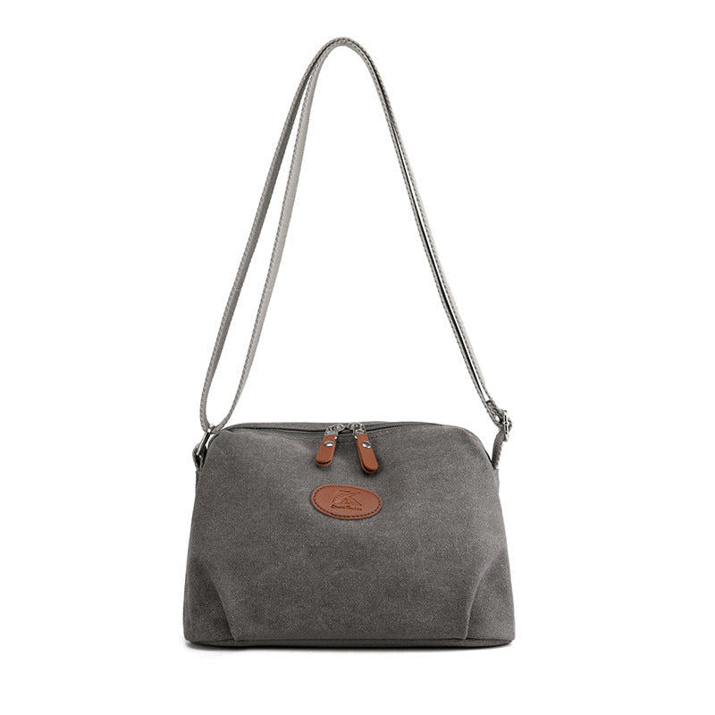 Borsa a tracolla in tela grigia con cerniera, dettagli in pelle marrone, design casual ed elegante, ideale per uso quotidiano e shopping.