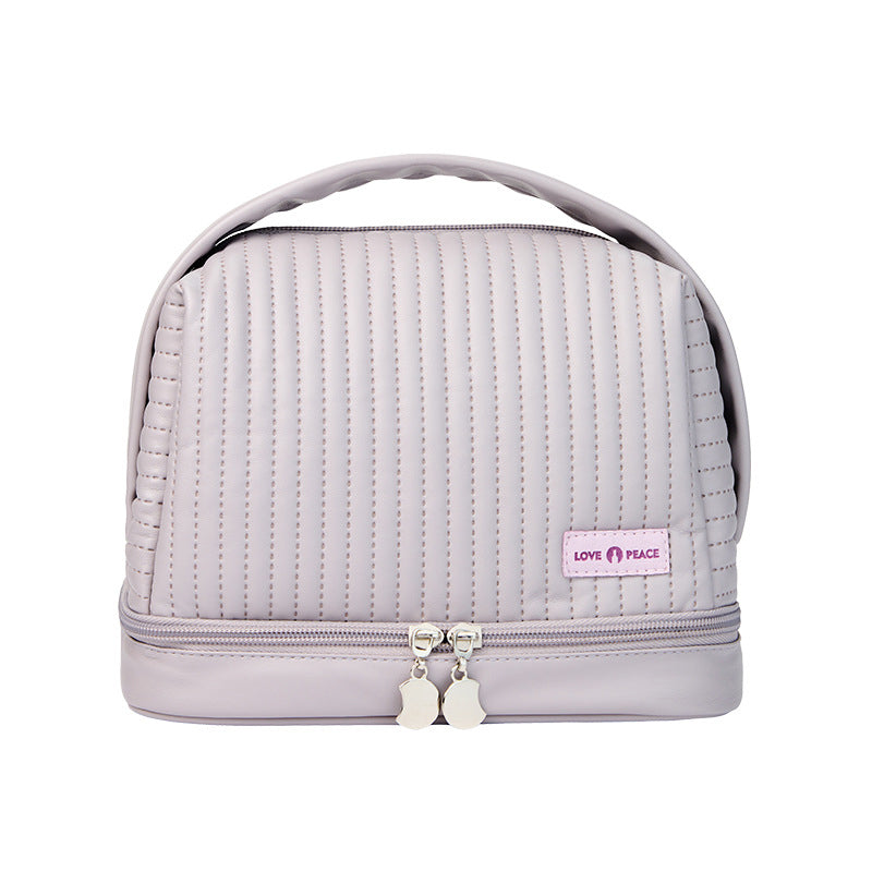 Borsa cosmetica trapuntata grigia con doppia zip, manico superiore e etichetta "Love Peace". Ideale per organizzare trucchi e accessori da viaggio.