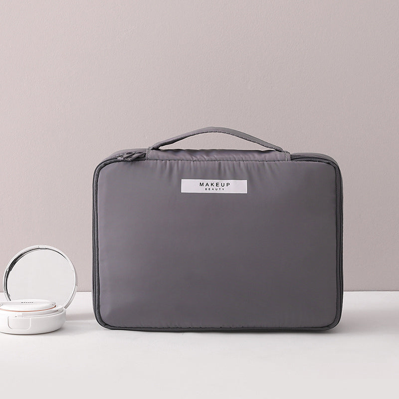 Borsa trucco grigia con manico, design elegante e compatto, ideale per organizzare cosmetici. Perfetta per viaggi e uso quotidiano.