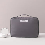 Borsa trucco grigia con manico, design elegante e compatto, ideale per organizzare cosmetici. Perfetta per viaggi e uso quotidiano.
