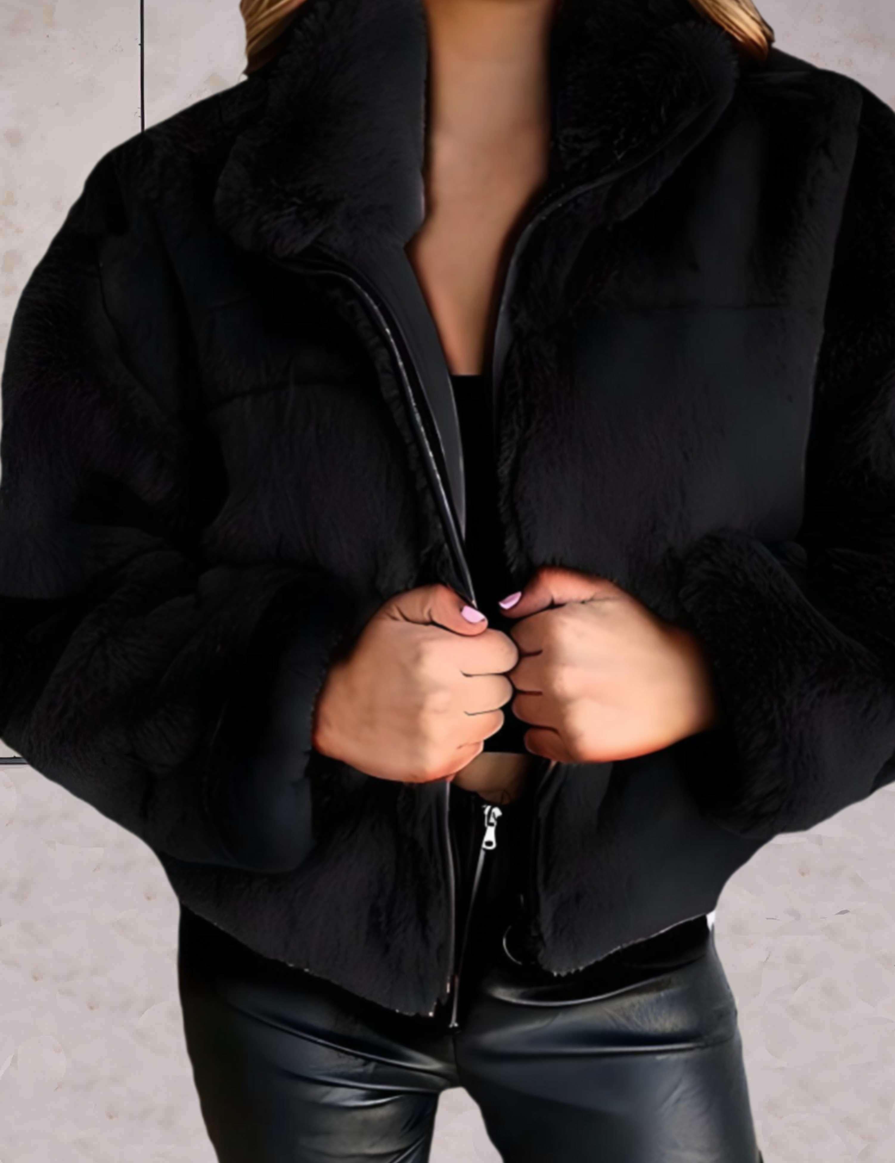 Giacca in ecopelliccia nera da donna, chiusura con zip, indossata su top nero e pantaloni in pelle. Moda invernale elegante e calda.