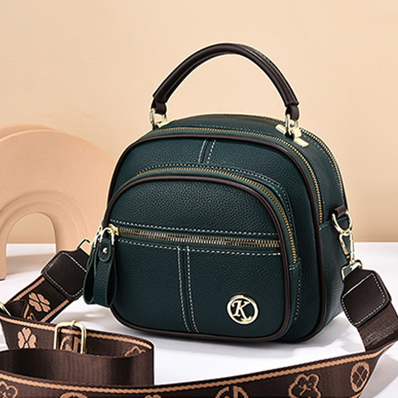 Borsa a tracolla in pelle verde scuro con manico superiore, cerniere dorate e tracolla regolabile marrone con motivo floreale. Elegante e versatile.