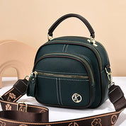 Borsa a tracolla in pelle verde scuro con manico superiore, cerniere dorate e tracolla regolabile marrone con motivo floreale. Elegante e versatile.