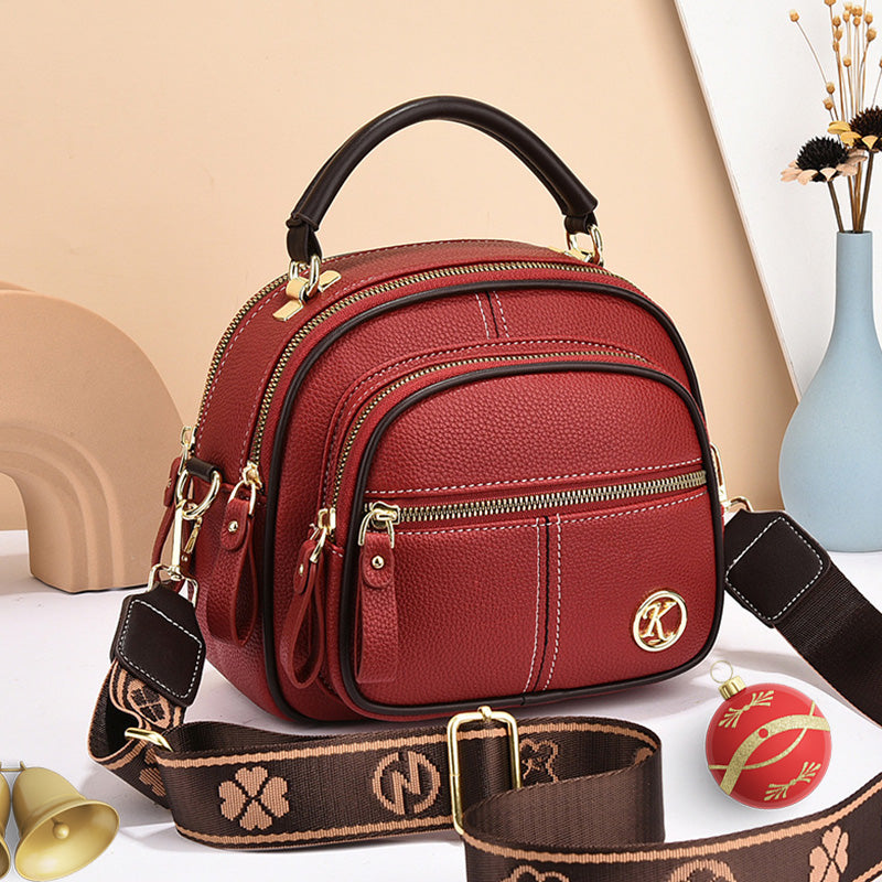 Borsa a tracolla rossa in pelle con manico nero, cerniere dorate, logo decorativo, e tracolla regolabile marrone. Accessorio moda elegante.