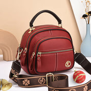 Borsa a tracolla rossa in pelle con manico nero, cerniere dorate, logo decorativo, e tracolla regolabile marrone. Accessorio moda elegante.