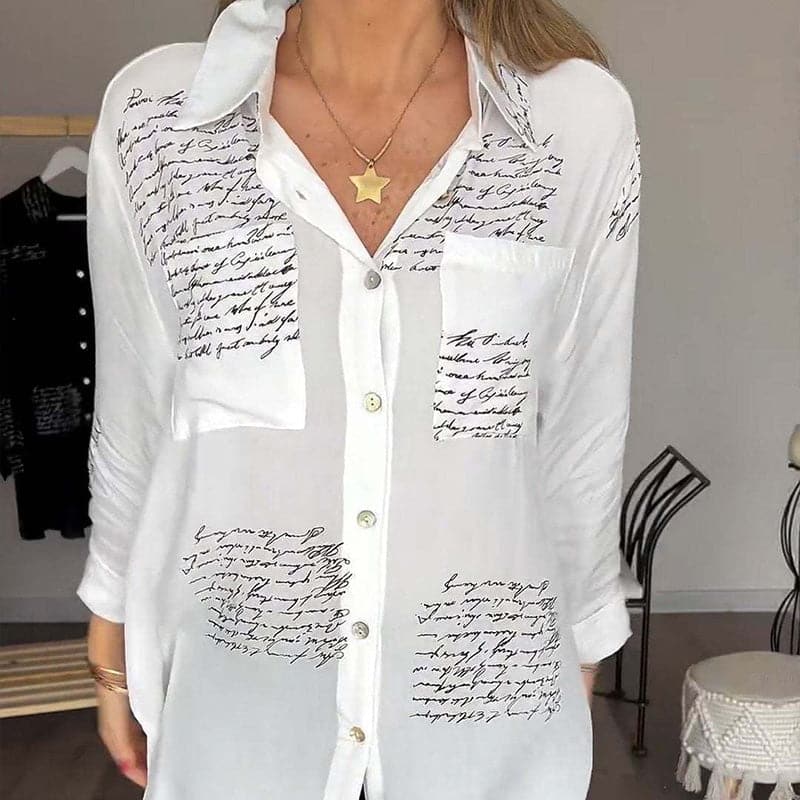 Camicia bianca da donna con scritte nere, maniche lunghe, colletto classico, tasca frontale, abbinata a collana con ciondolo a stella. Moda casual elegante.