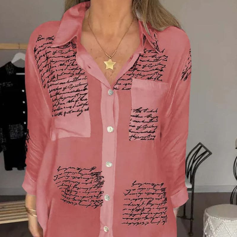 Camicia donna rosa con scritte nere, maniche lunghe, colletto classico, bottoni frontali, tasca sul petto, stile casual elegante.