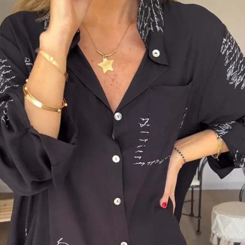 Camicia nera da donna con scritte bianche, maniche lunghe, abbinata a collana con ciondolo a stella e bracciali dorati. Moda casual elegante.