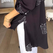 Camicia nera con scritte bianche, maniche lunghe, abbinata a pantaloni bianchi. Moda casual elegante, tessuto leggero, stile moderno.