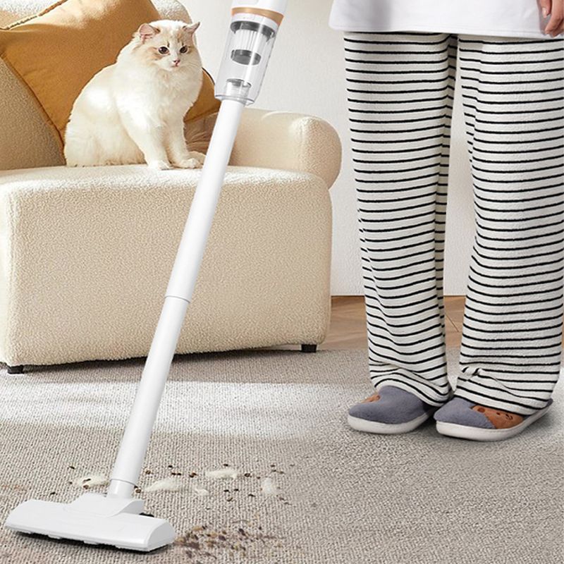 Aspirapolvere senza fili bianco su tappeto beige, accanto a persona in pigiama a righe e gatto bianco su divano. Pulizia casa, elettrodomestico moderno.