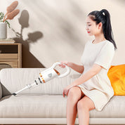 Donna seduta su divano beige utilizza aspirapolvere portatile bianco per pulizia domestica; design moderno, efficienza, comodità.