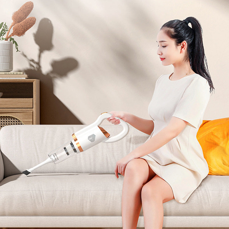Donna seduta su divano beige utilizza aspirapolvere portatile bianco per pulizia domestica; design moderno, efficienza, comodità.