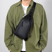Uomo con borsa a tracolla nera in pelle, indossa camicia verde. Accessorio moda maschile, elegante e pratico per uso quotidiano.