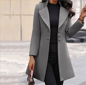Donna con cappotto grigio elegante, abbinato a maglia nera e pantaloni, in contesto urbano. Moda autunnale, stile sofisticato.