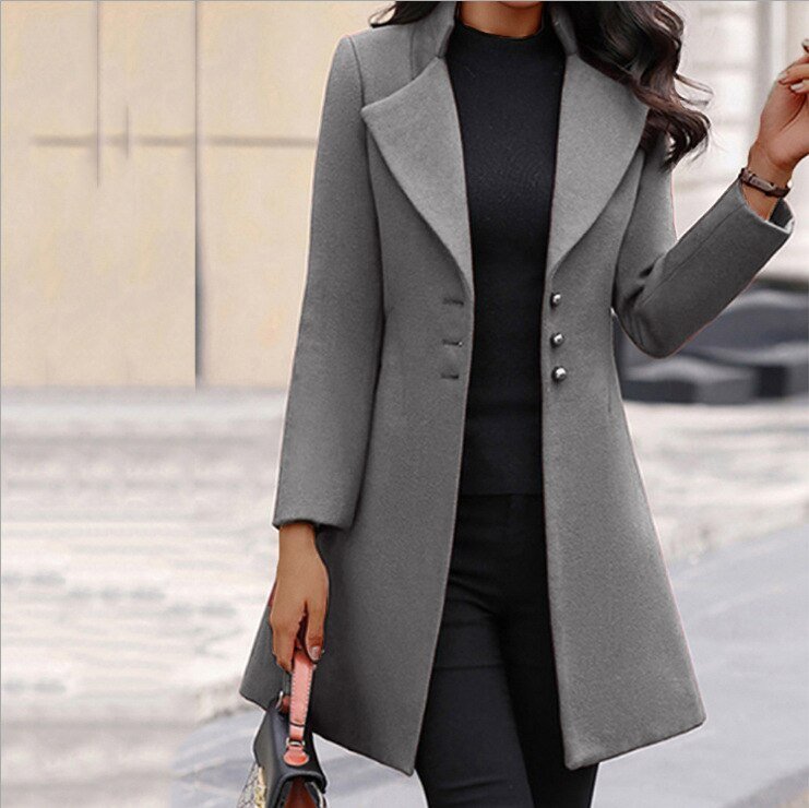Donna con cappotto grigio elegante, abbinato a maglia nera e pantaloni, in contesto urbano. Moda autunnale, stile sofisticato.