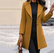 Cappotto lungo donna giallo senape, elegante, con bottoni, abbinato a maglia nera e pantaloni scuri. Moda autunnale, stile sofisticato.