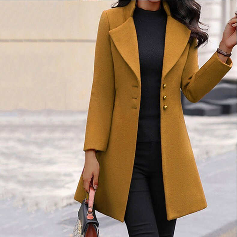Cappotto lungo donna giallo senape, elegante, con bottoni, abbinato a maglia nera e pantaloni scuri. Moda autunnale, stile sofisticato.