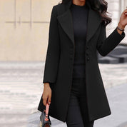 Donna con cappotto nero elegante, abbinato a maglia e pantaloni neri, tiene una borsa. Look autunnale chic e sofisticato.