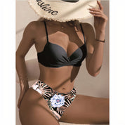 Donna in bikini nero con slip a fantasia floreale, indossa cappello di paglia. Moda mare, costumi da bagno eleganti, estate, spiaggia.