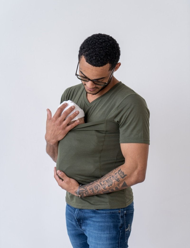 Uomo con tatuaggio indossa maglietta verde e jeans, tiene un biberon bianco nel taschino. Sfondo bianco. Accessori per neonati, cura del bambino.