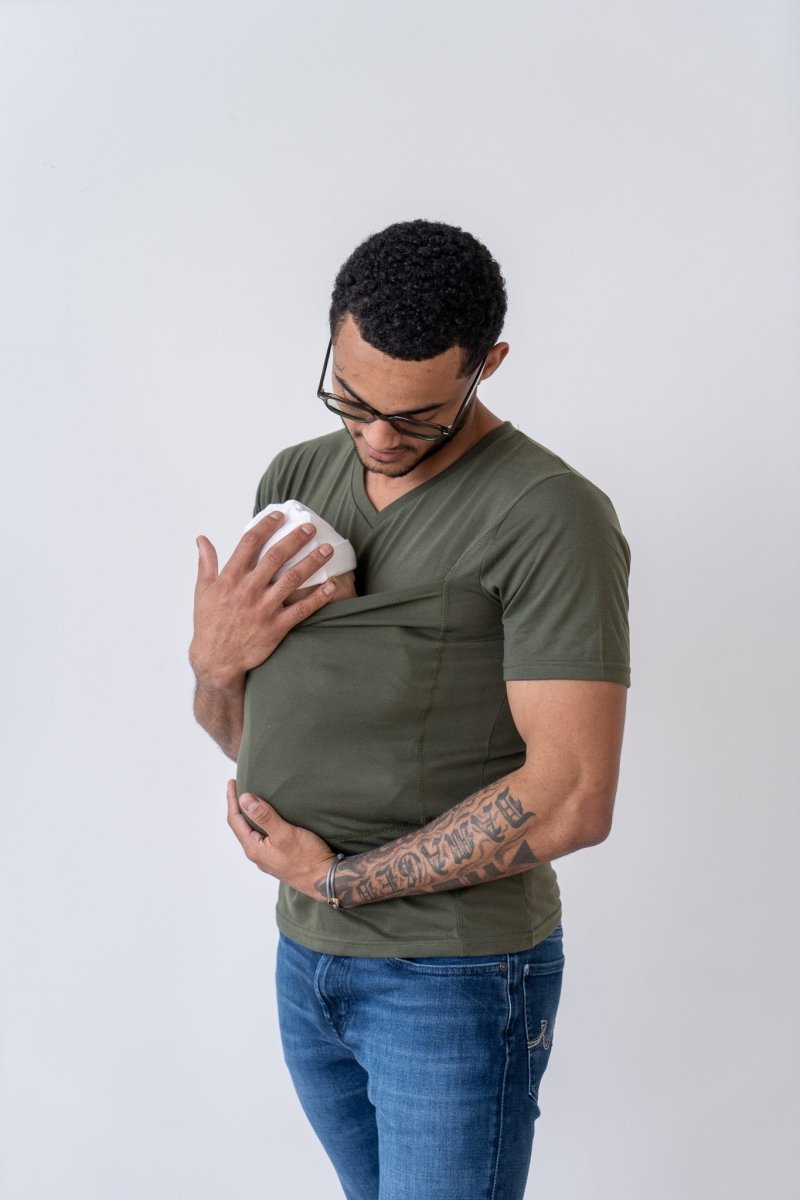Uomo con tatuaggio indossa maglietta verde e jeans, tiene un biberon bianco nel taschino. Sfondo bianco. Accessori per neonati, cura del bambino.