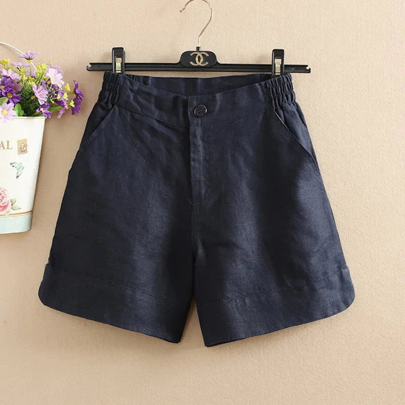 Pantaloncini donna in lino blu scuro, con elastico in vita e tasche laterali, appesi su gruccia nera. Eleganti e casual, ideali per l'estate.