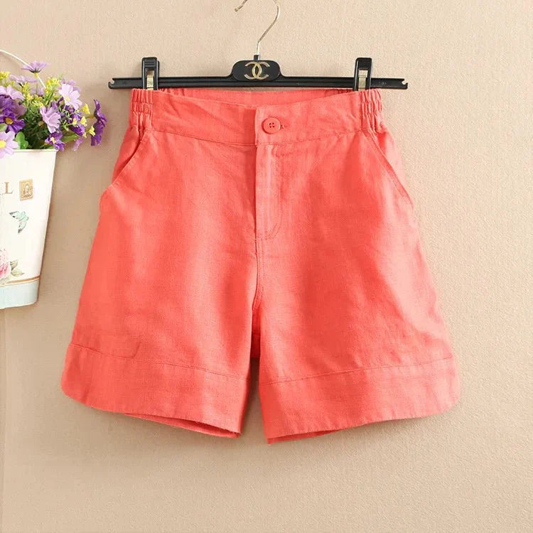 Pantaloncini donna in lino rosa corallo, elasticizzati in vita, con tasche laterali, appesi su gruccia. Ideali per estate e moda casual.