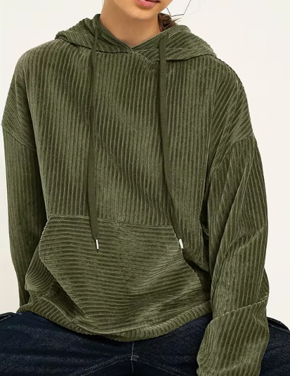 Felpa verde oliva a coste con cappuccio e tasca frontale, indossata da una persona seduta. Stile casual, tessuto morbido e confortevole.