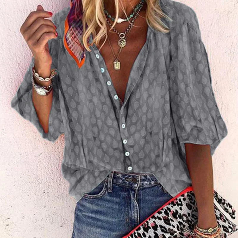 Blusa grigia a maniche lunghe con motivo a pois, abbinata a jeans blu. Accessori: collane, bracciali e pochette leopardata. Moda casual donna.