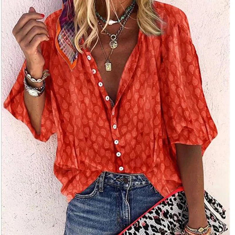 Camicia donna arancione a maniche corte con motivo, abbinata a jeans. Accessori: collane, bracciali, foulard colorato. Stile casual estivo.