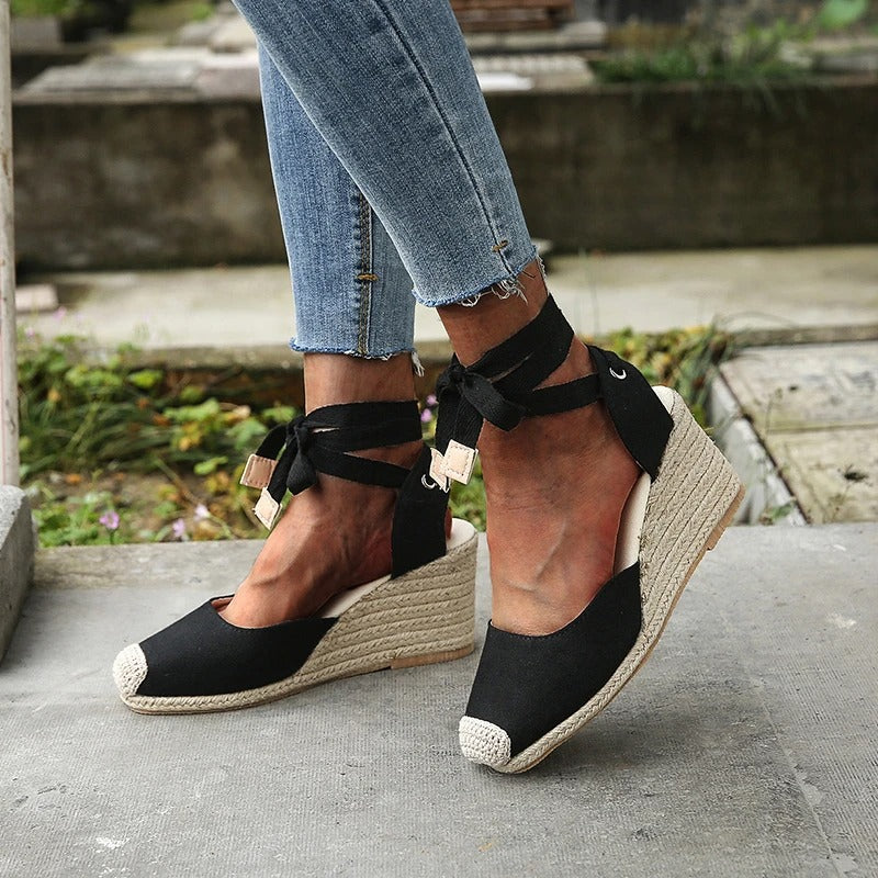 Scarpe espadrillas nere con zeppa in corda, lacci alla caviglia, indossate con jeans. Calzature estive eleganti e casual per donna.